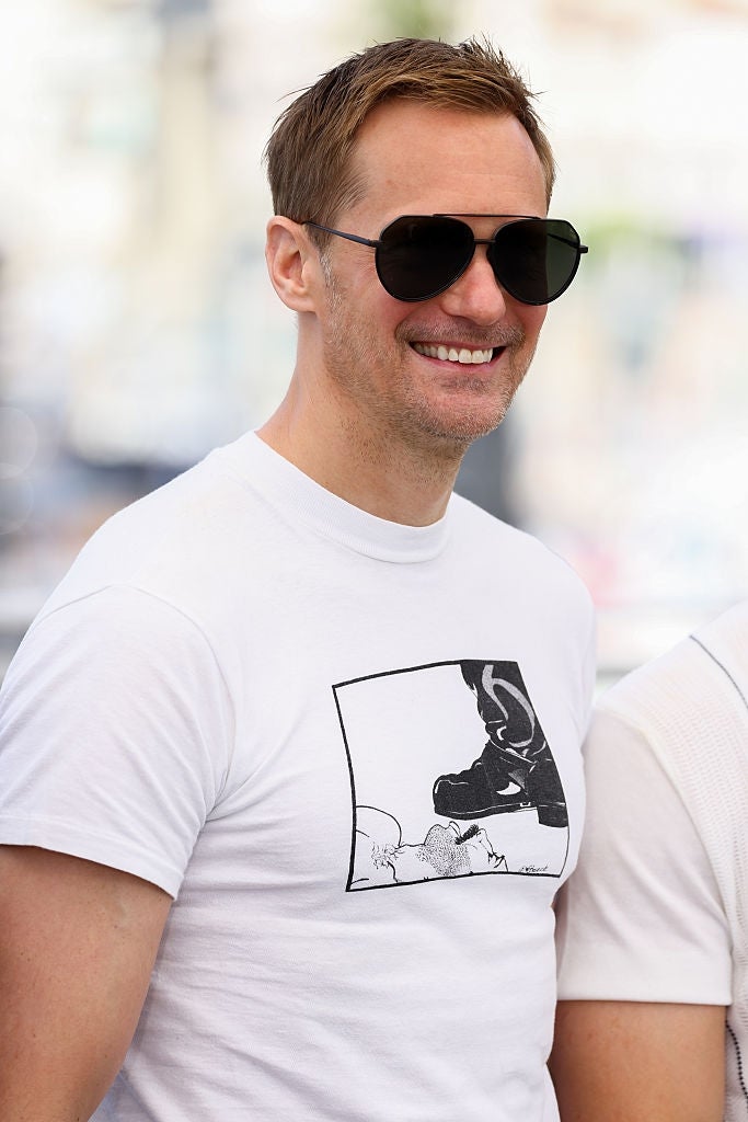 Person smiling, wearing a graphic T-shirt with a footwear illustration and acheronian sunglasses, lasting outdoors during the day