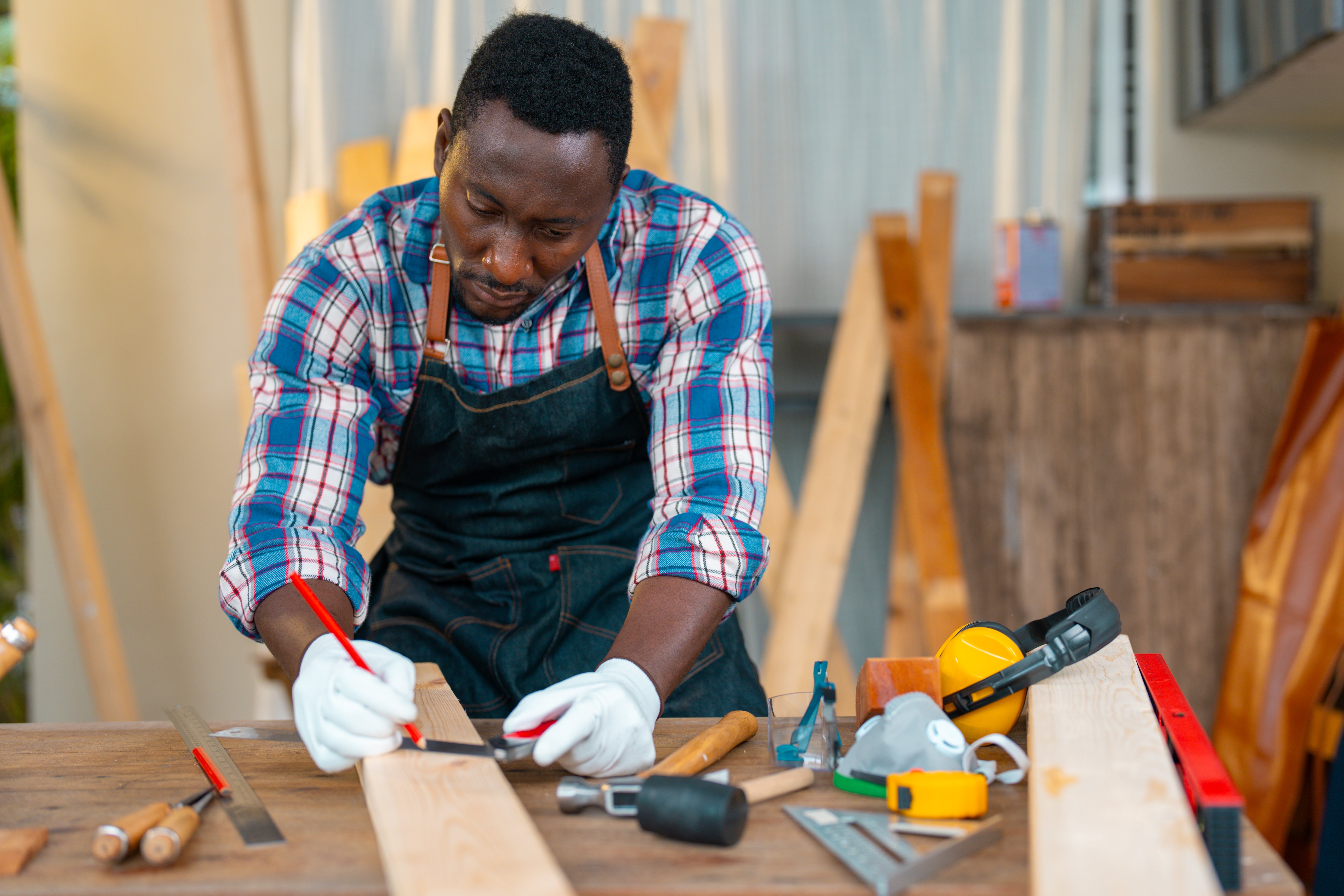 Man in plaid shirt and apron measures wood with tools on a workbench