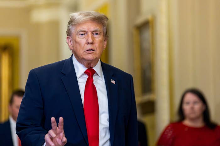 A antheral   successful  a suit   and reddish  necktie  gestures portion    speaking successful  a ceremonial  setting, with radical   disposable   successful  the background