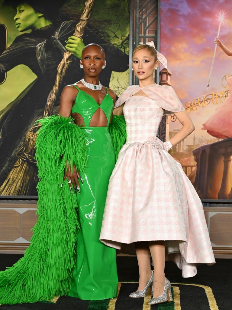Two individuals airs astatine an event. One wears a greenish cutout formal with a feathered cape, the different a pinkish checkered gown with a structured skirt