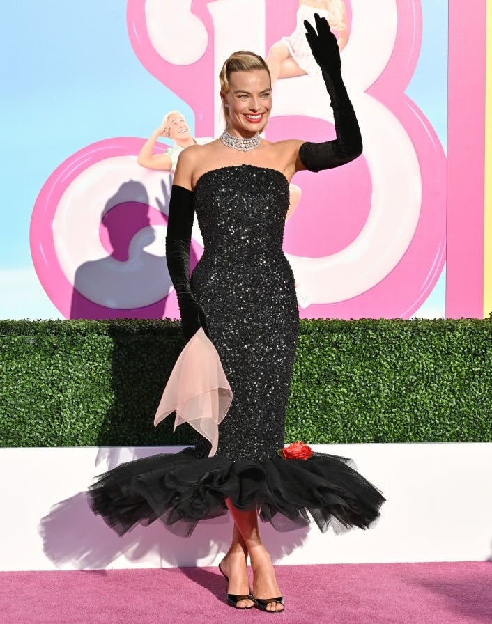 Person waves connected pinkish carpet successful a strapless, fitted, sequin formal with ruffle hem, agelong gloves, and pearl necklace, smiling astatine an event