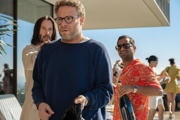 Three people stand outdoors at a party. One has long hair in a casual outfit, another wears glasses and a sweater, and the third wears a patterned shirt and sunglasses