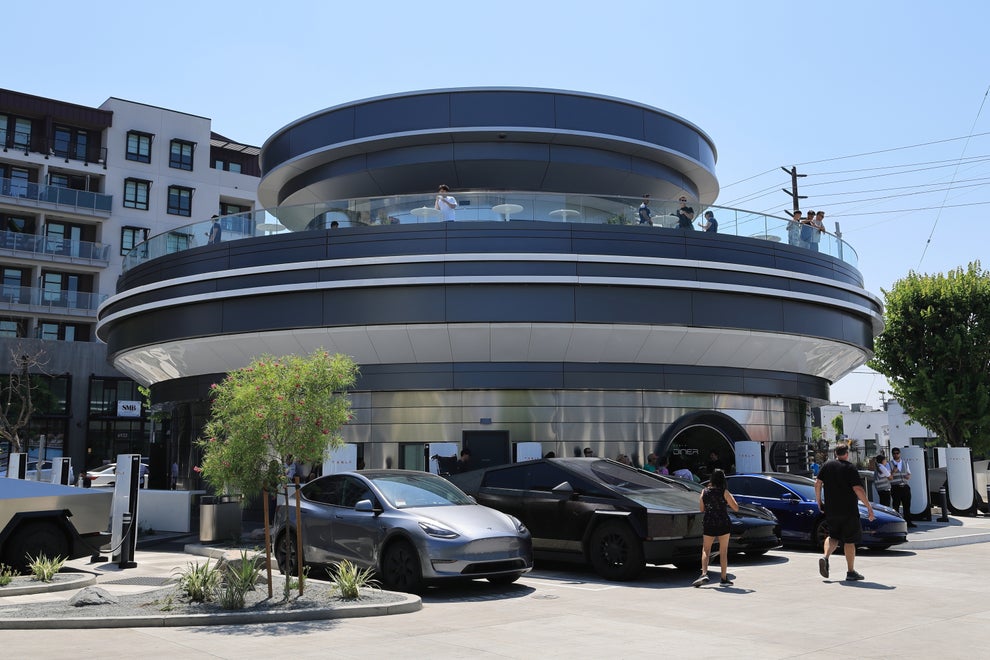 A modern, circular building with a futuristic design, surrounded by parked electric vehicles, and people walking nearby