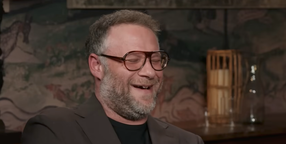 A person with glasses laughing in a cozy indoor setting