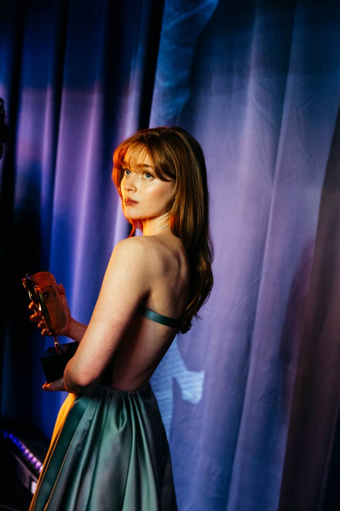 Person successful  an elegant backless gown holding an award, lasting  successful  beforehand   of a curtain