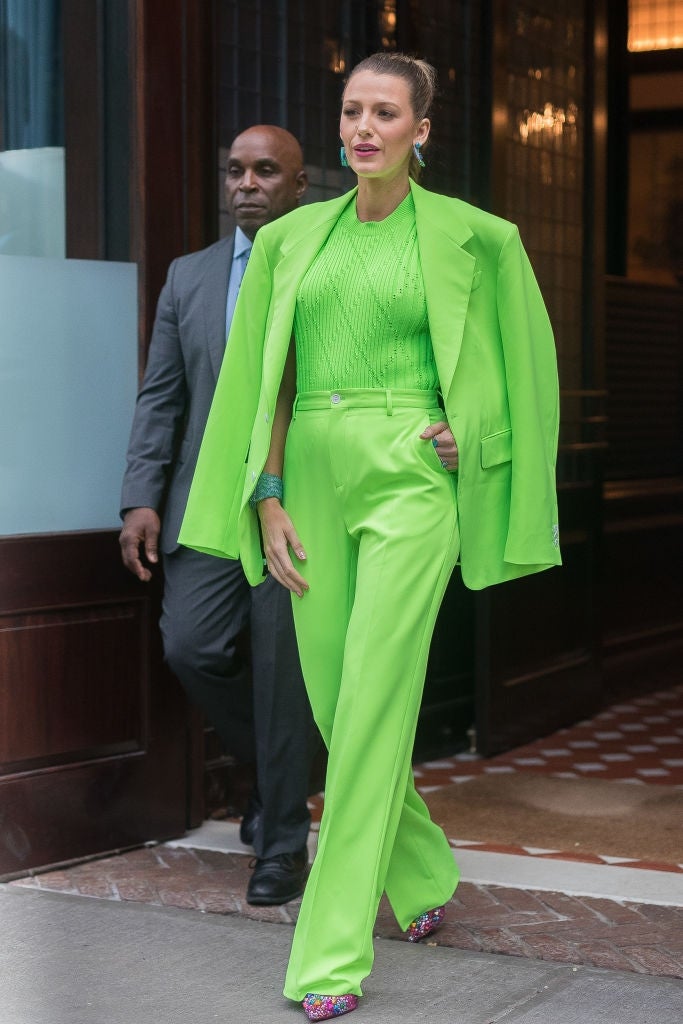 Person wearing a bright, stylish monochrome suit with embellished shoes, walking with a information defender successful the background
