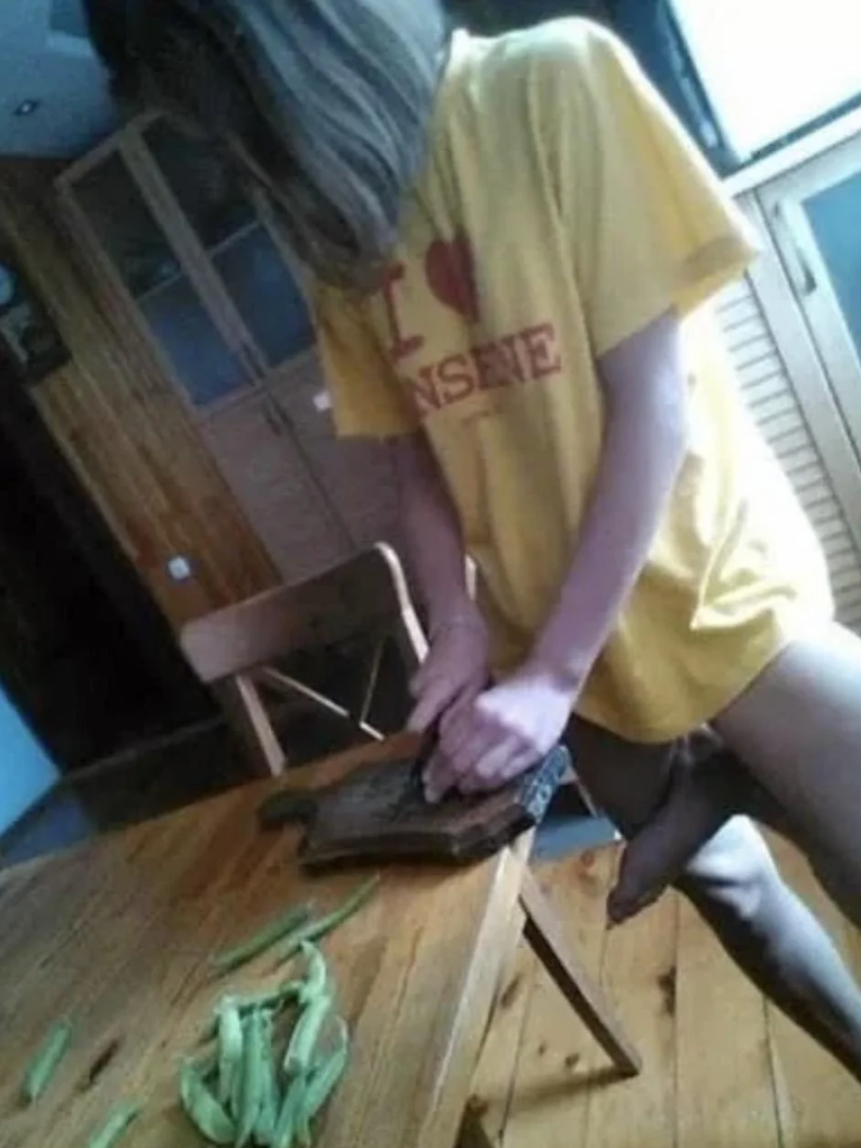 Person chopping vegetables on a wooden board in a kitchen, wearing a yellow T-shirt with text on it