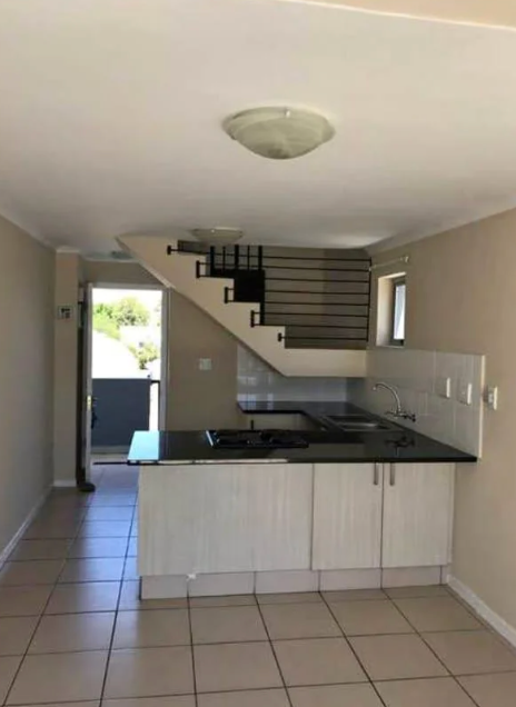 Modern kitchen area with tiled floor, a counter with stovetop, and a staircase leading to the upper level. Doorway visible in the background
