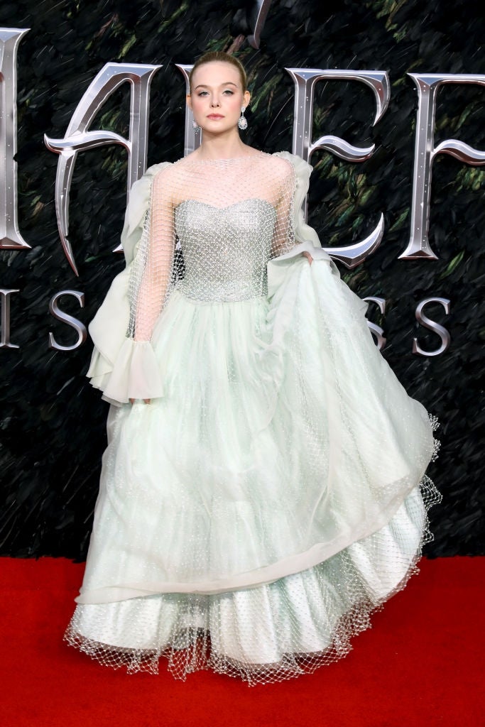 Person successful an elegant gown with sheer sleeves and layered skirt connected the reddish carpet, posing confidently successful beforehand of a backdrop