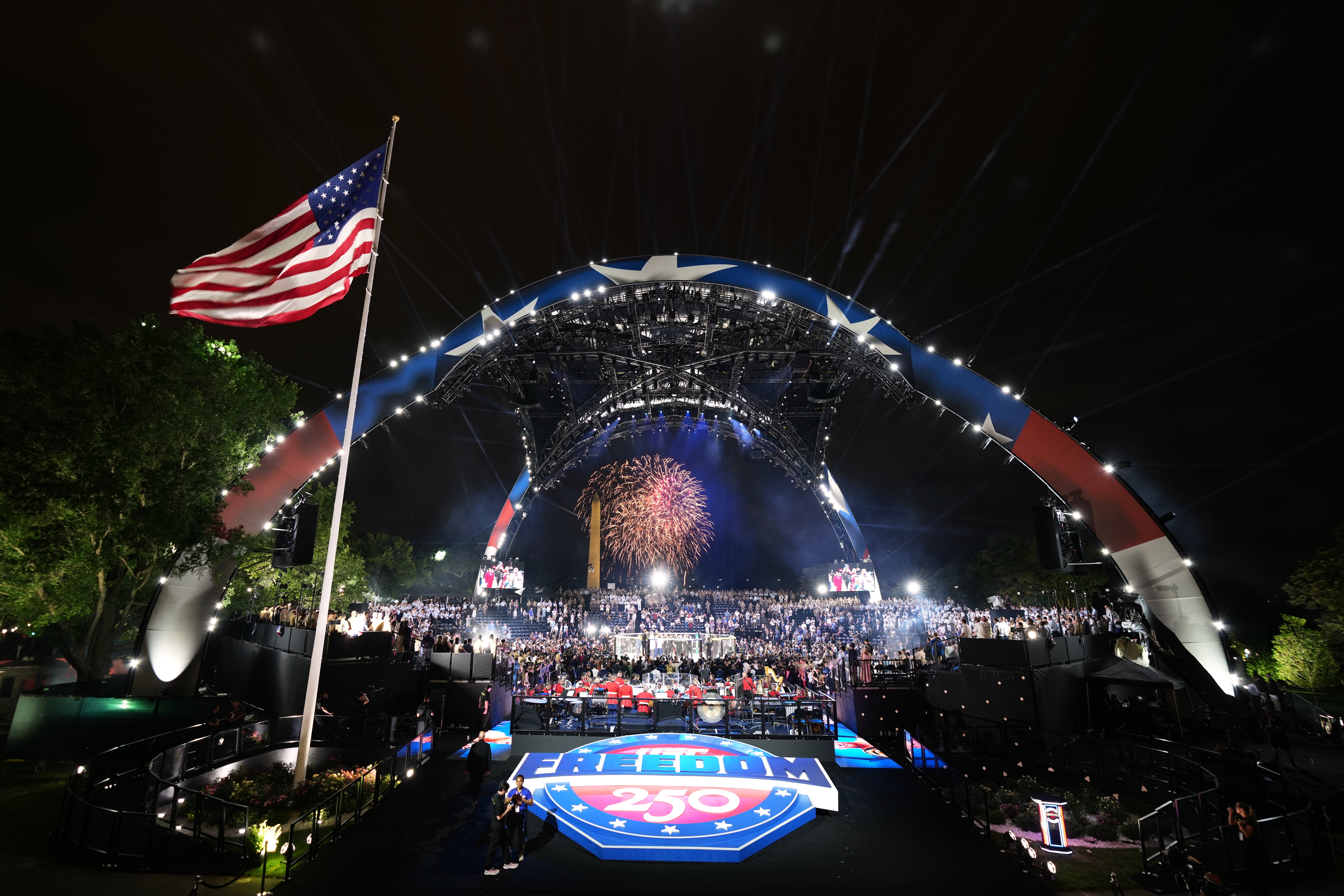 Nighttime outdoor performance with a ample arched stage, fireworks successful the background, and an American emblem waving successful the foreground