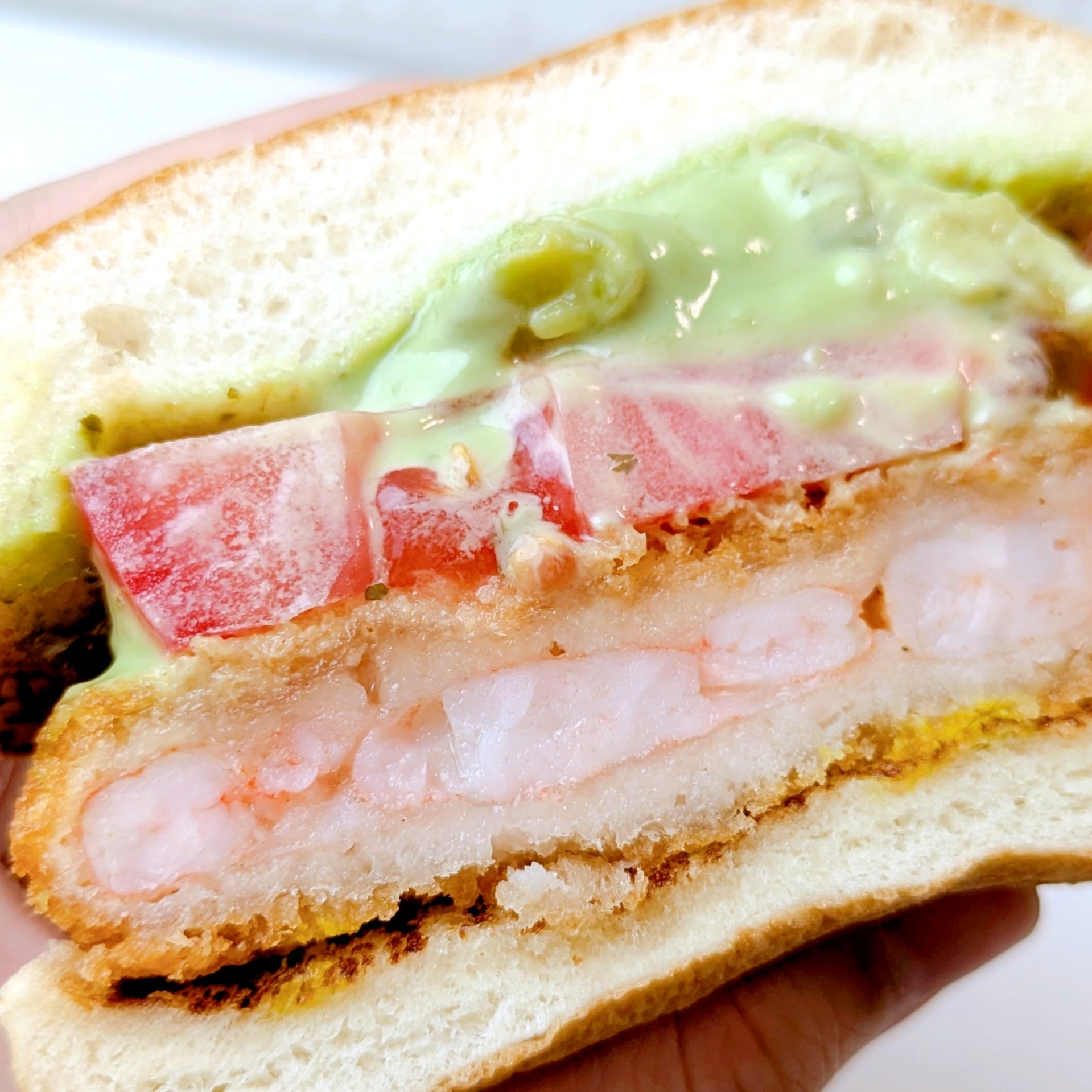 モスバーガー「アボカド海老カツバーガー ～国産バジルマヨ～」ハンバーガーのカット断面。海老カツ、トマト、ソースが見える。