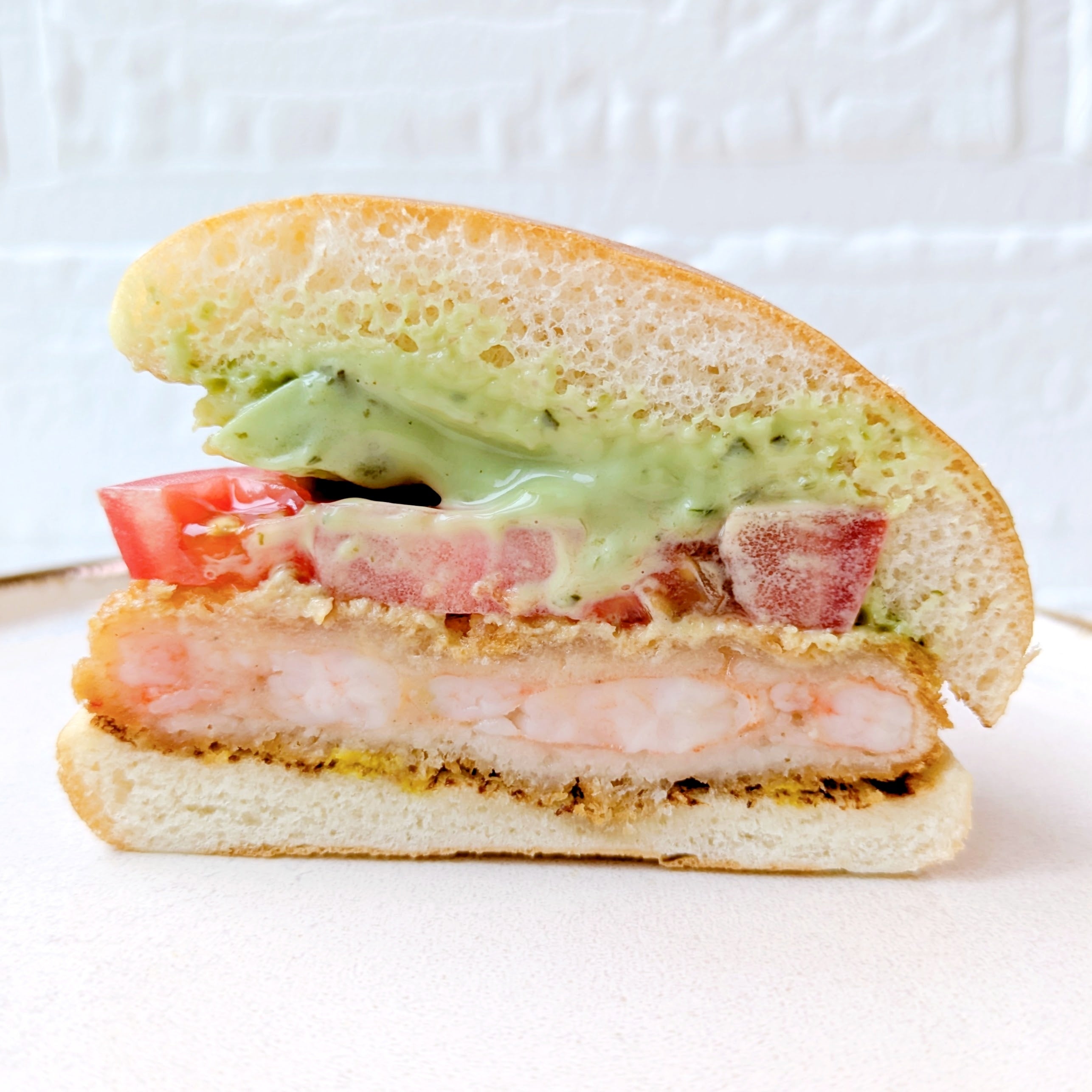 モスバーガー「アボカド海老カツバーガー ～国産バジルマヨ～」海老カツ、トマト、アボカド、バジルソース入りのハンバーガーの断面。