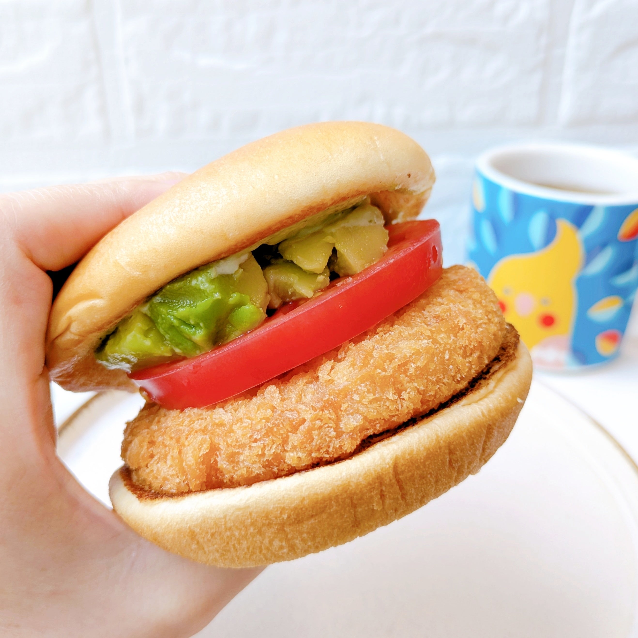 モスバーガー「アボカド海老カツバーガー ～国産バジルマヨ～」手に持たれたハンバーガー、アボカドとトマト入り。