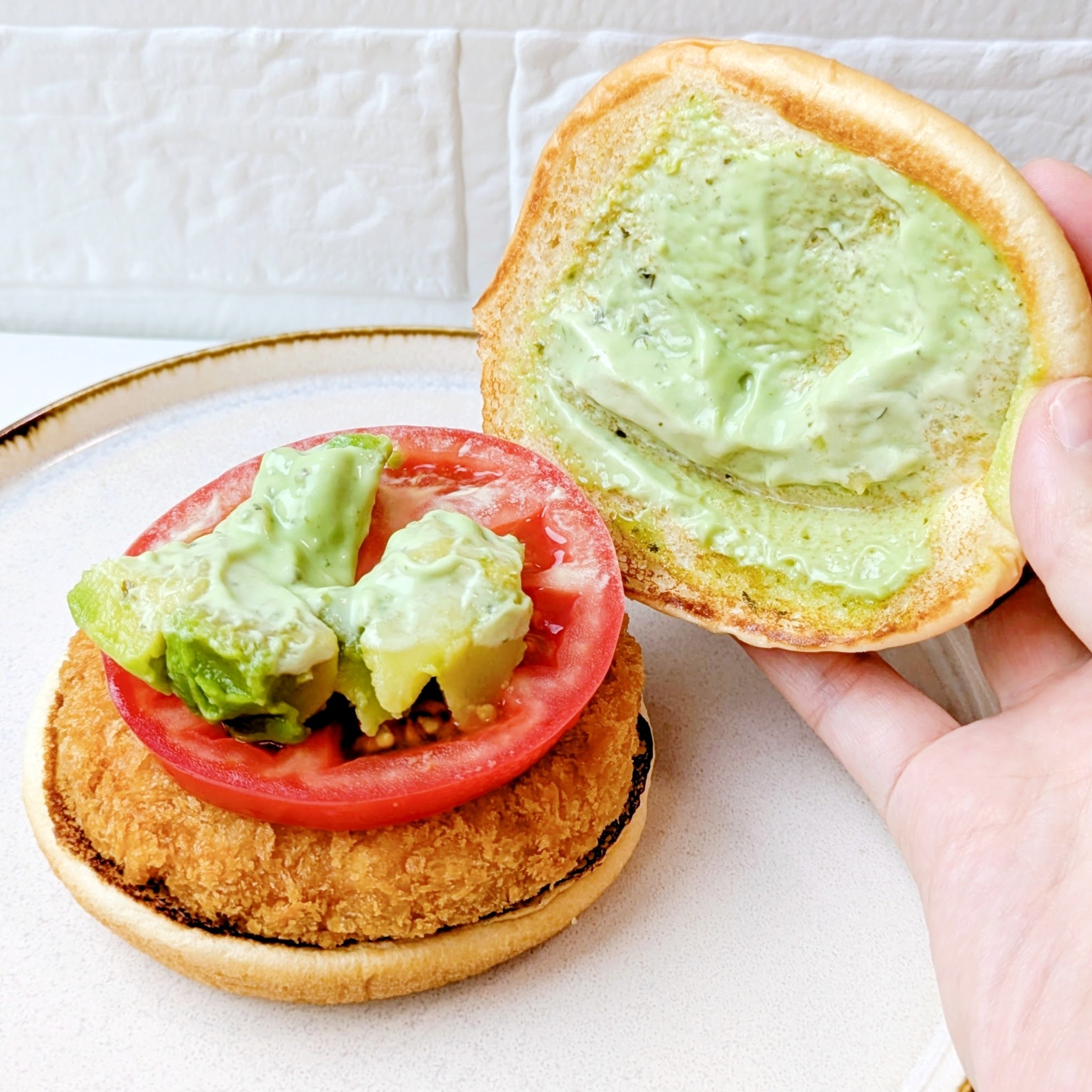 モスバーガー「アボカド海老カツバーガー ～国産バジルマヨ～」海老カツ、トマト、アボカド、ソースがのったハンバーガーが皿にのっている。