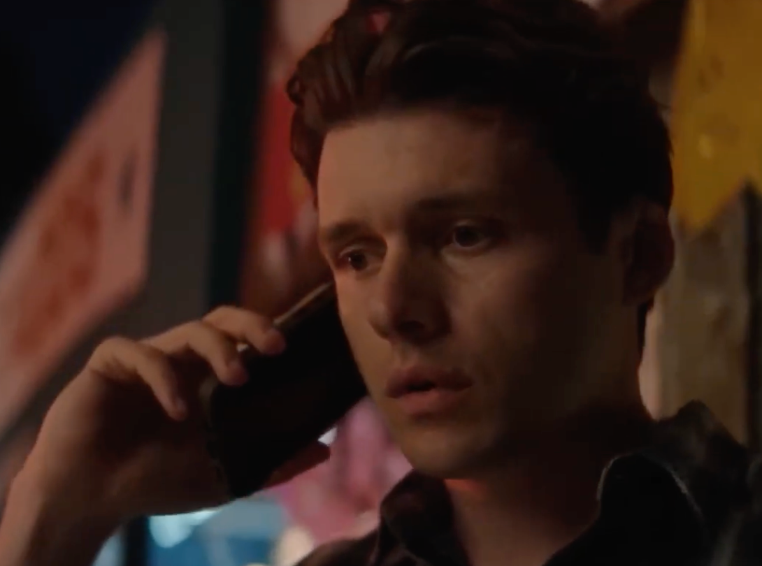 A person is talking on a cellphone, looking concerned. The background appears to be blurred, suggesting an urban setting