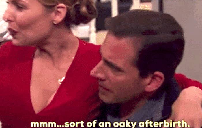 A man in a suit tastes wine at an event, commenting humorously about its flavor