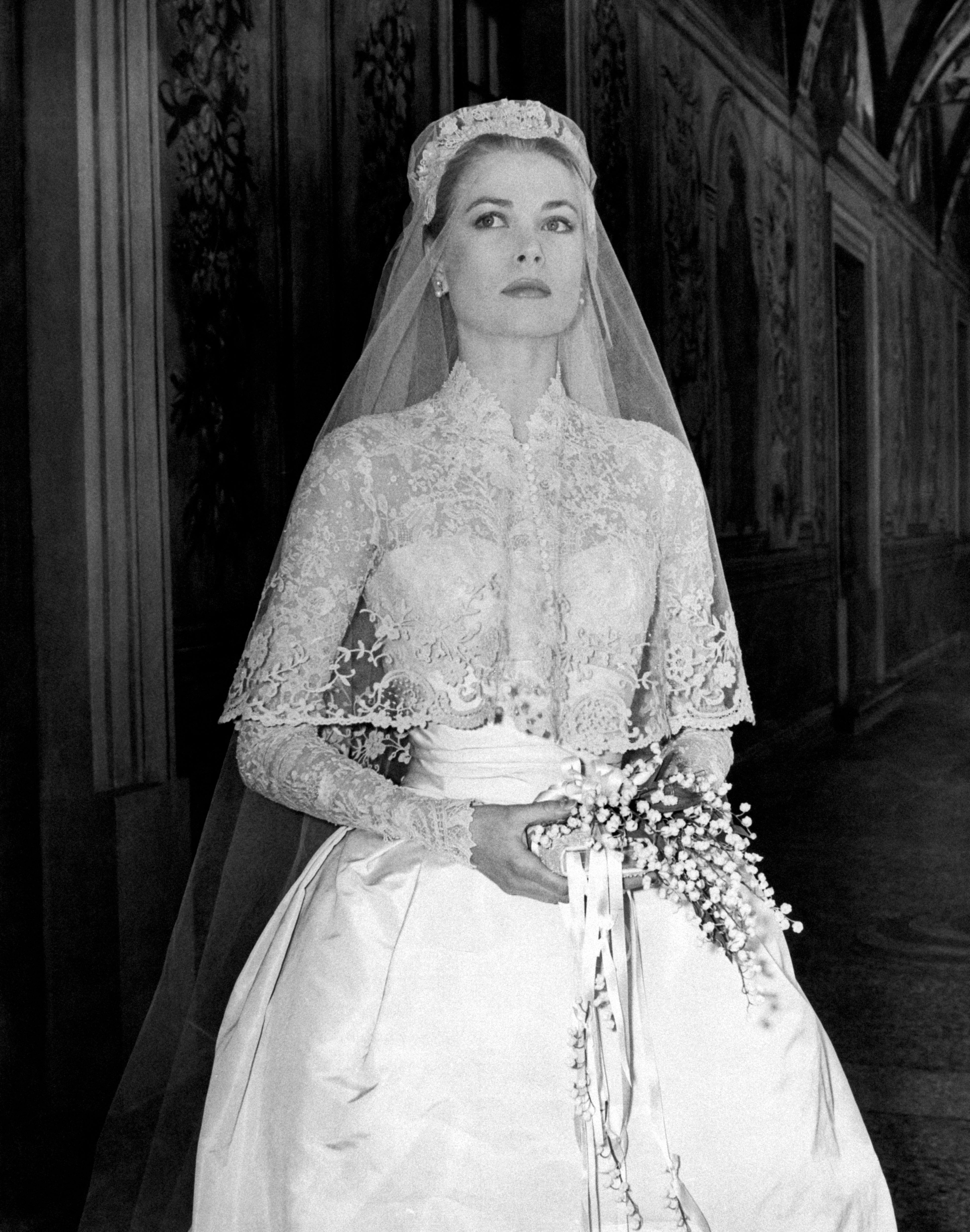 Bride in lace wedding gown with a long veil holds a bouquet, posing elegantly