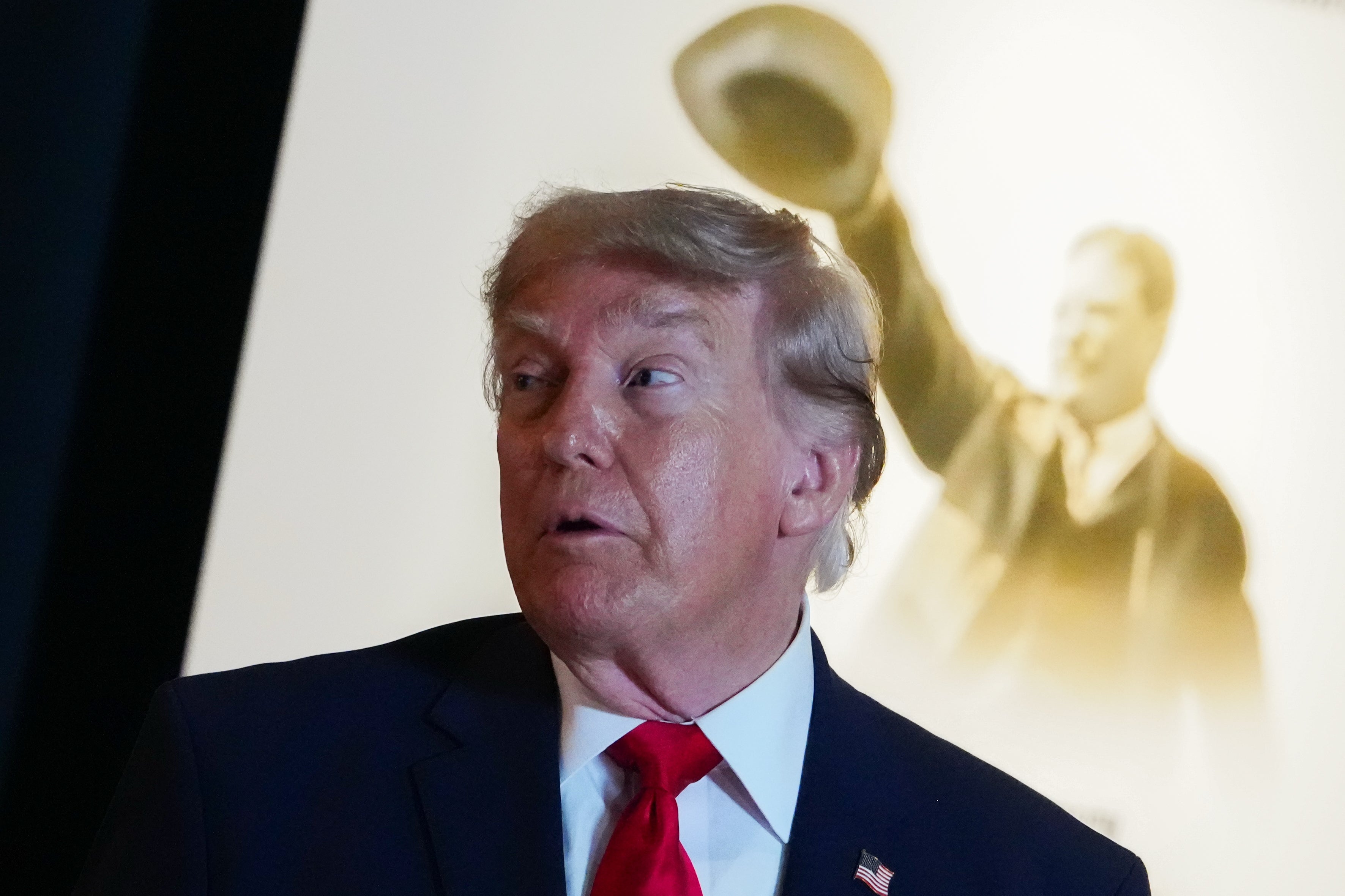 A idiosyncratic successful a suit with a reddish necktie appears to talk successful beforehand of a backdrop featuring a humanities fig raising a hat