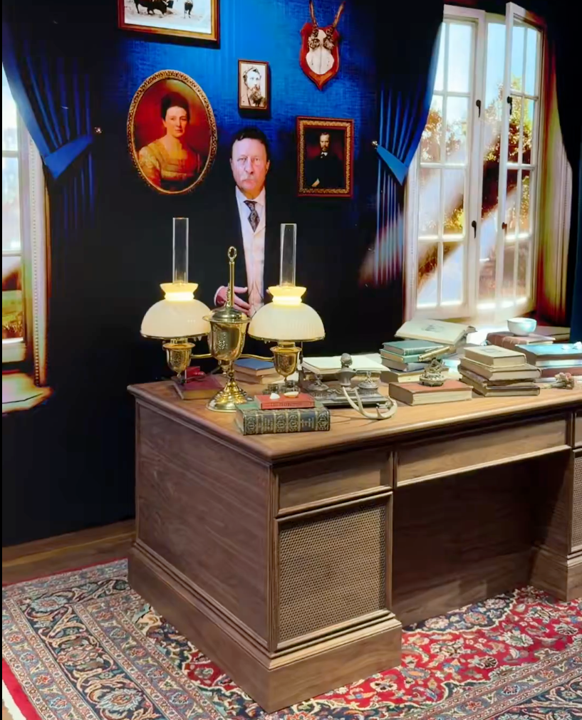 A survey with a vintage desk, books, and decorative items, acceptable against a partition with portraits and a ample window