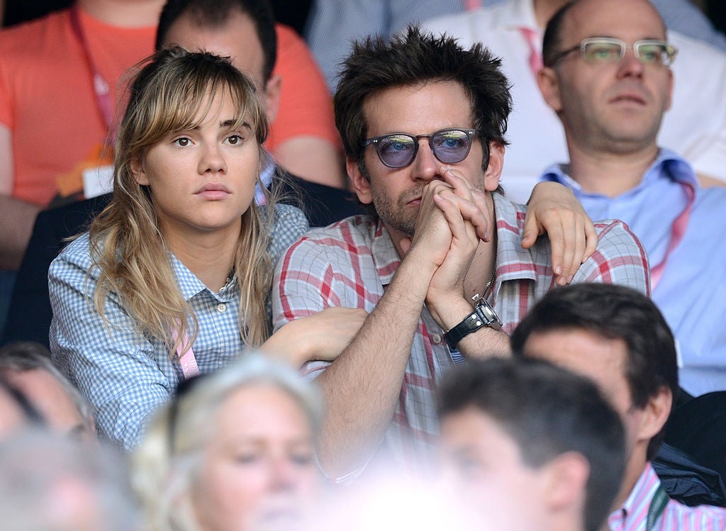 Suki Waterhouse sits with her arm around Bradley Cooper watching a tennis match