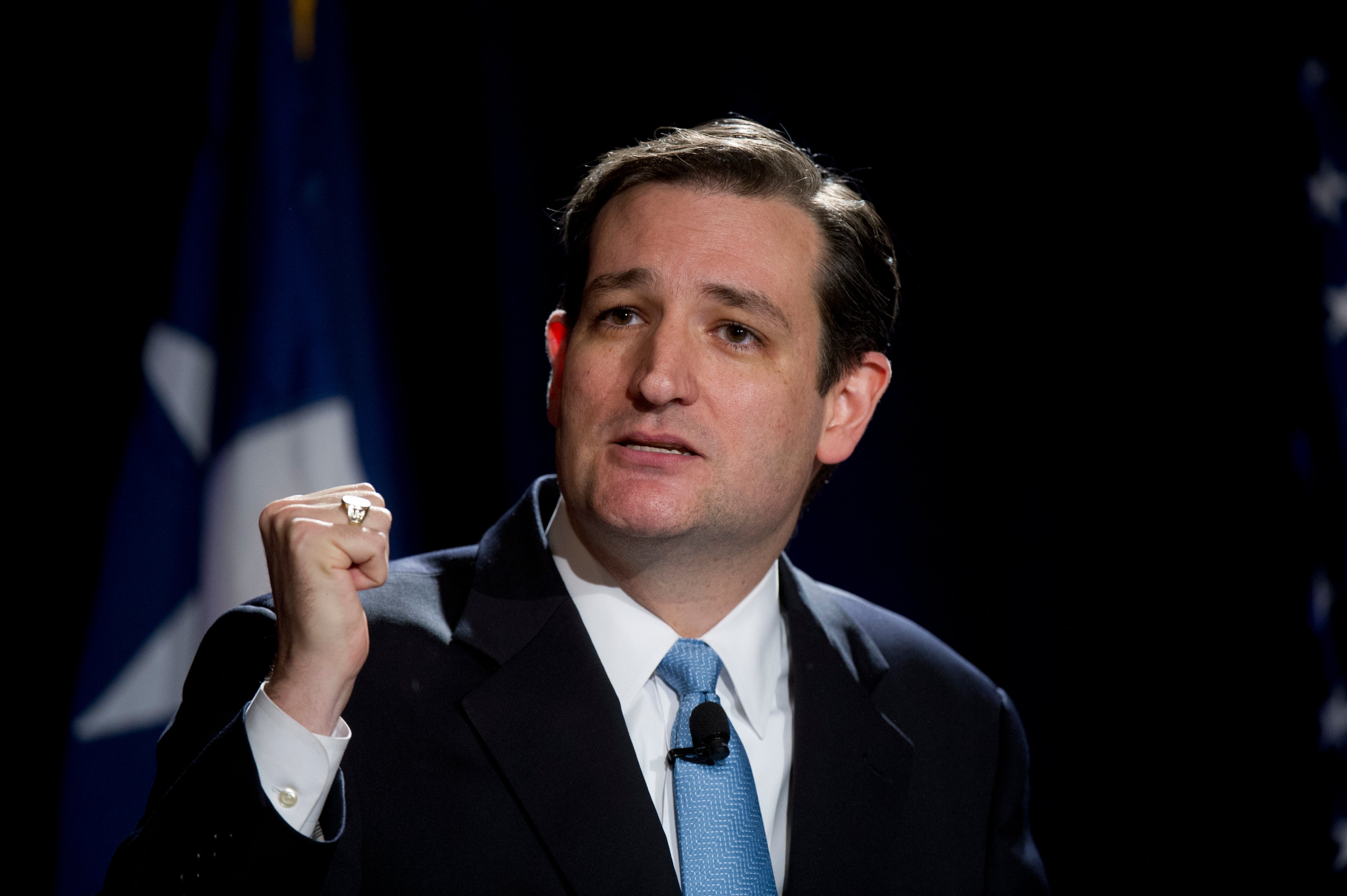 A idiosyncratic successful a suit gestures portion speaking astatine an event, with a Texas emblem partially disposable successful the background
