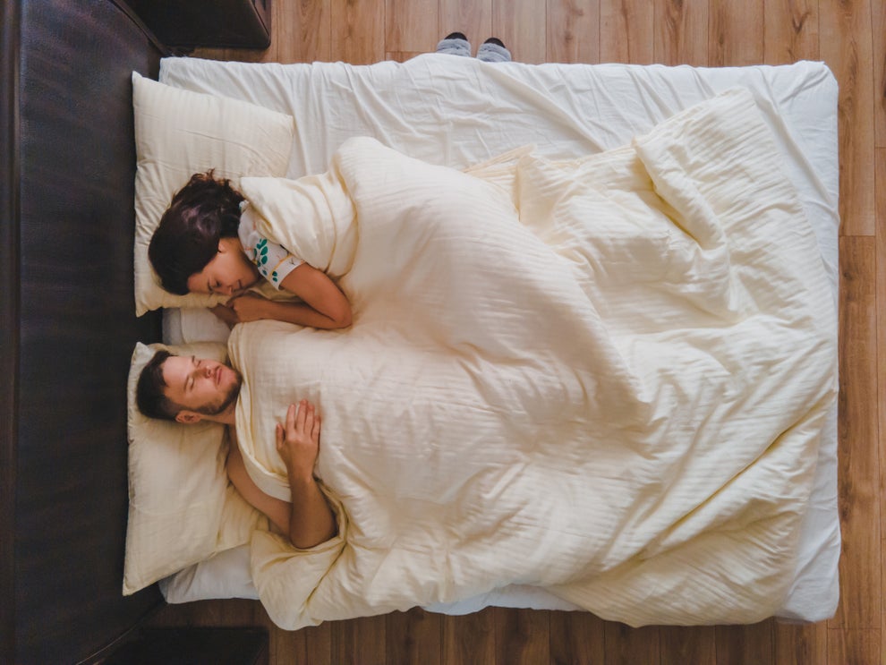 A couple lying in bed under a blanket, facing each other, suggesting intimacy and connection