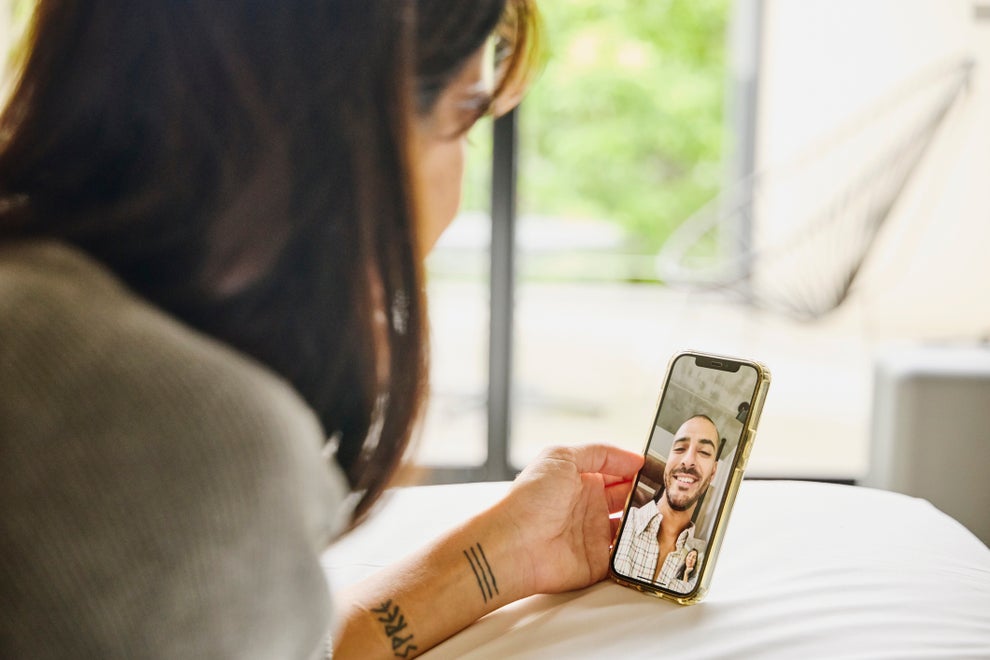 A person video chats with a smiling person on a smartphone, both appearing relaxed and engaged, suggesting a romantic connection