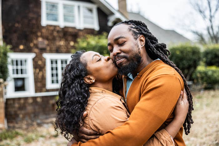 A couple shares a tender kiss outdoors, embracing affectionately in front of a house