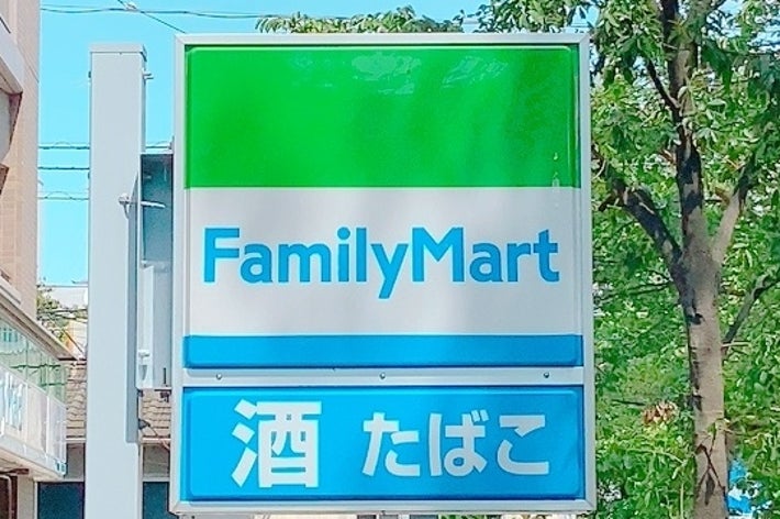 ファミリーマートの看板。酒やたばこを取り扱っていることを示す。建物と木が背景に見える。