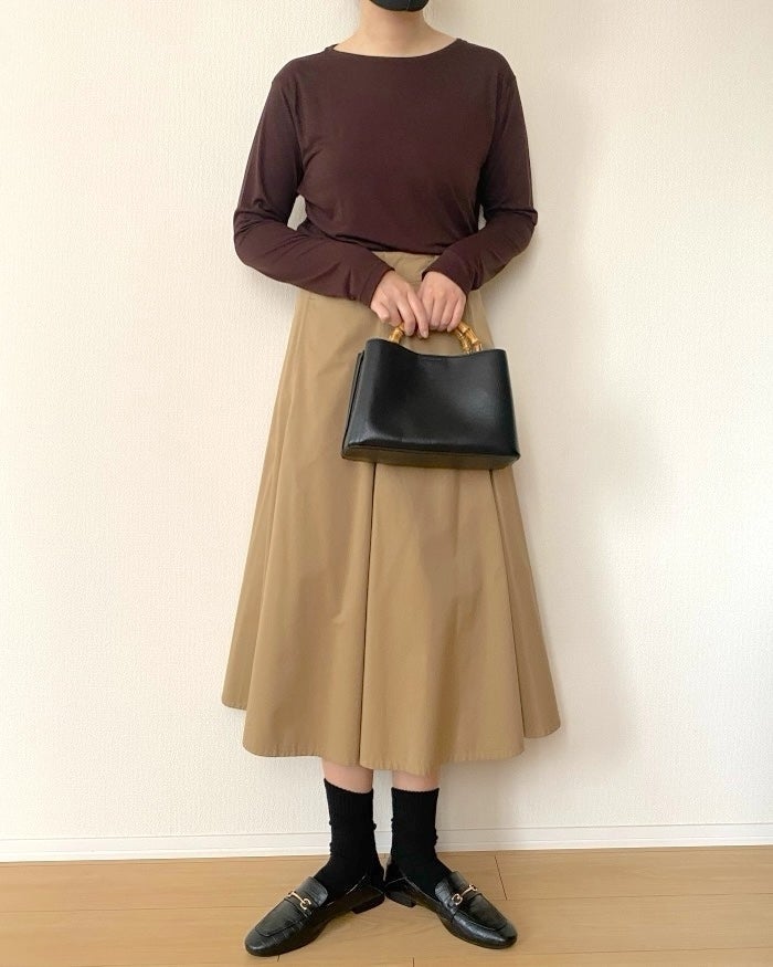 UNIQLO（ユニクロ）の「シアーT」女性が黒いバッグとローファー、茶色のトップス、ベージュのミディスカートを着用している。