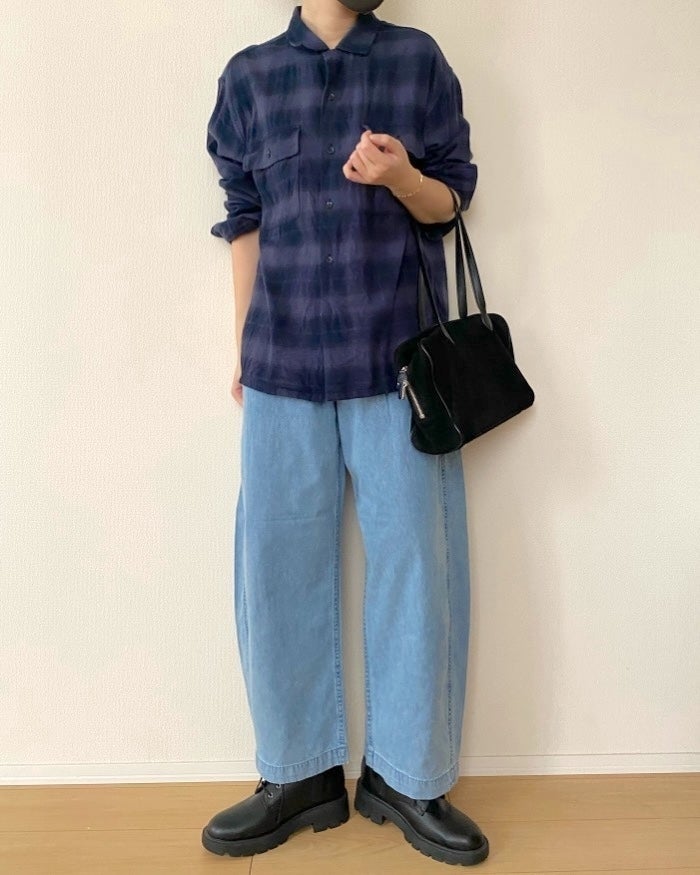 GUの「ライトデニムバレルレッグイージーパンツ（丈標準67.5～71.5cm）」人物がゆったりとしたデニムパンツとチェック柄のシャツを着てポーズを取り、ブラックのアクセサリーバッグを持っています。