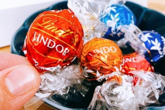 手に持たれたリンドールチョコレートと、いくつかのチョコが皿に盛られている。