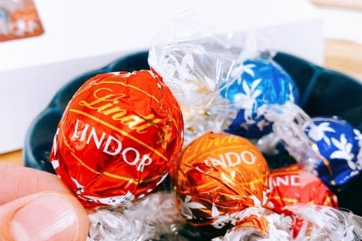 手に持たれたリンドールチョコレートと、いくつかのチョコが皿に盛られている。