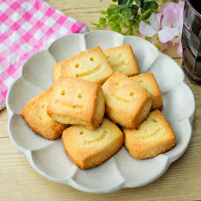お皿に笑顔の形をしたクッキーが盛られている。後ろに花と市松模様の布が見える。