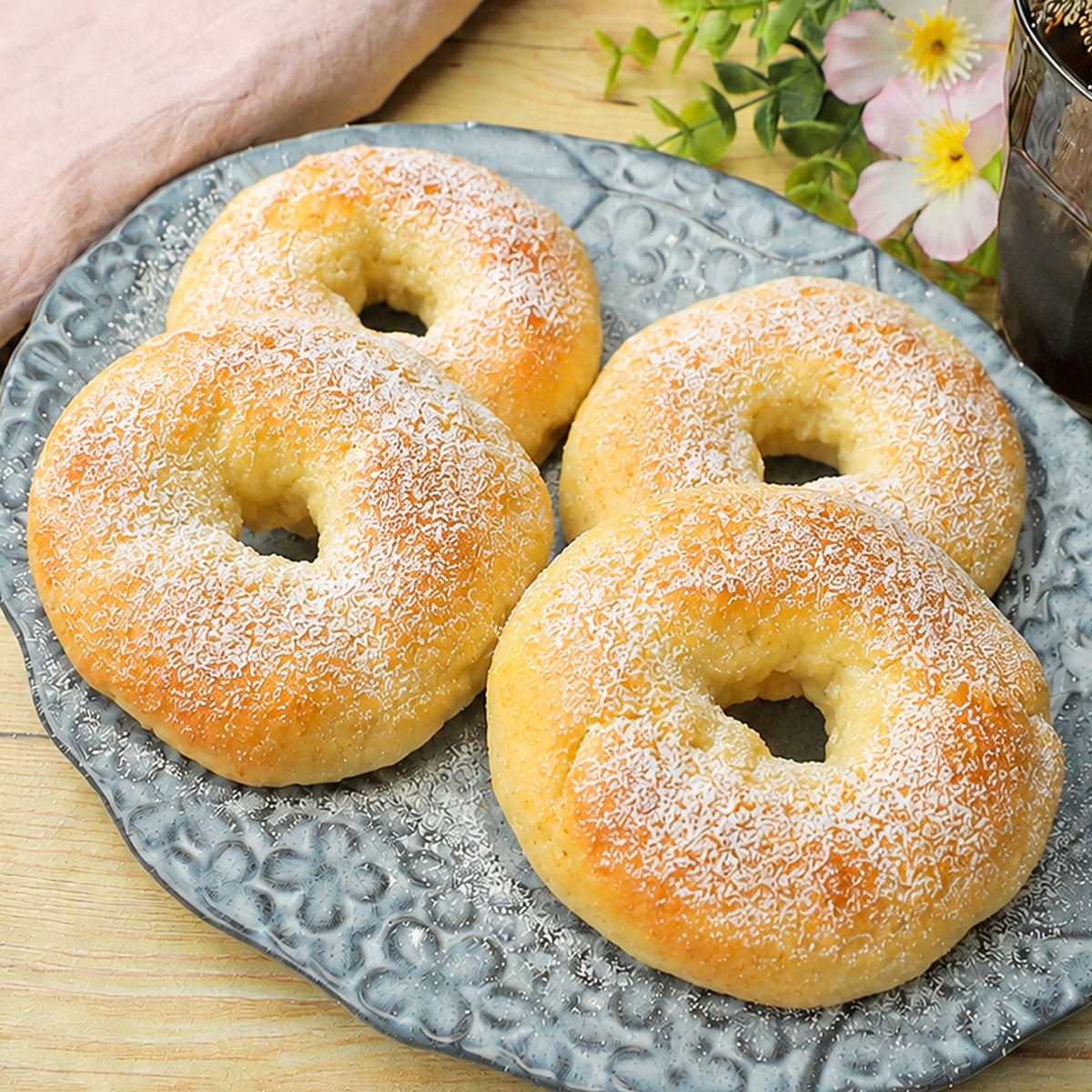お皿に4つの焼きたてのベーグルが乗っている。上に粉砂糖がかかっている。