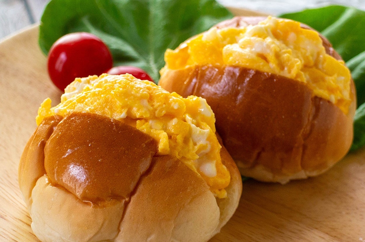 皿にフワフワのスクランブルエッグが乗った2つのパンが並んでおり、葉物とトマトが添えられています。