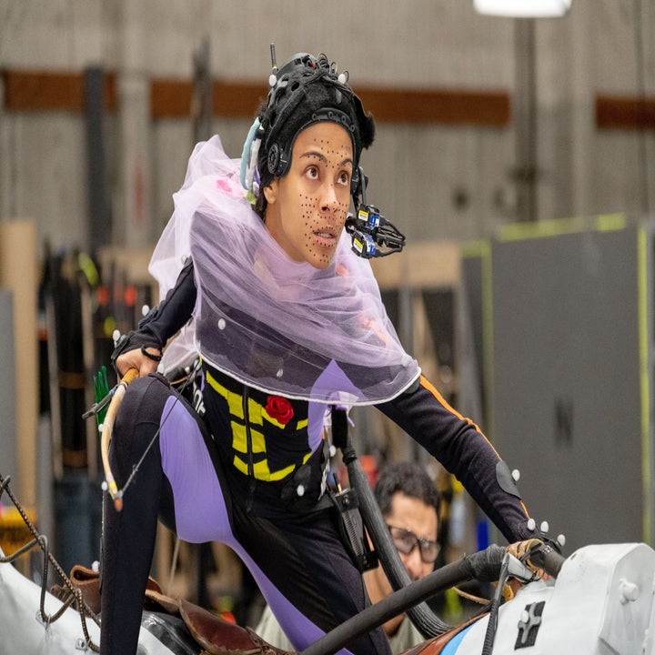 Zoe Saldana wearing a motion capture suit with facial markers. She is posed in a crouched position, focused on the task