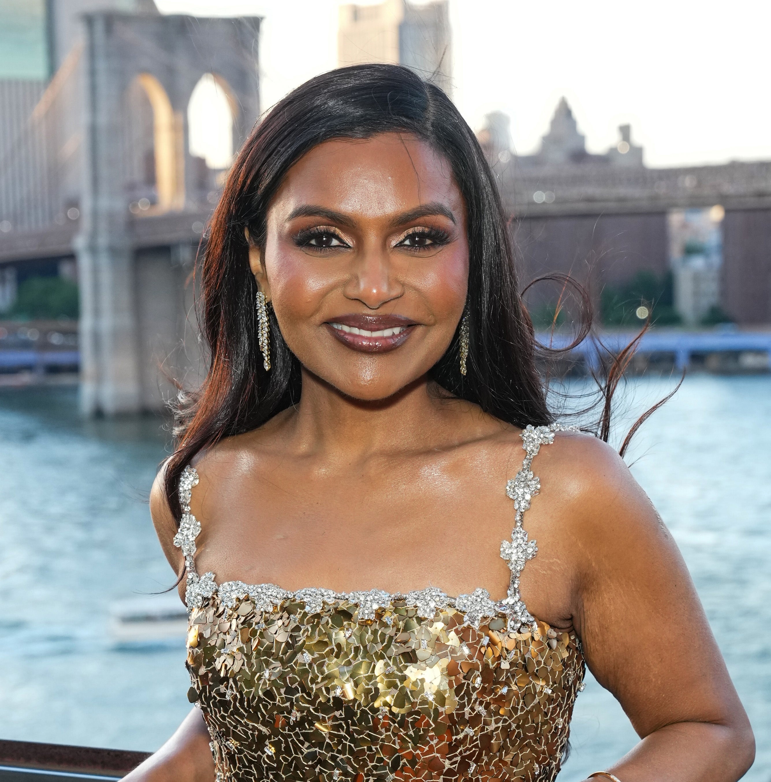 Person in a glittering gown with floral details stands in front of a cityscape featuring a famous bridge