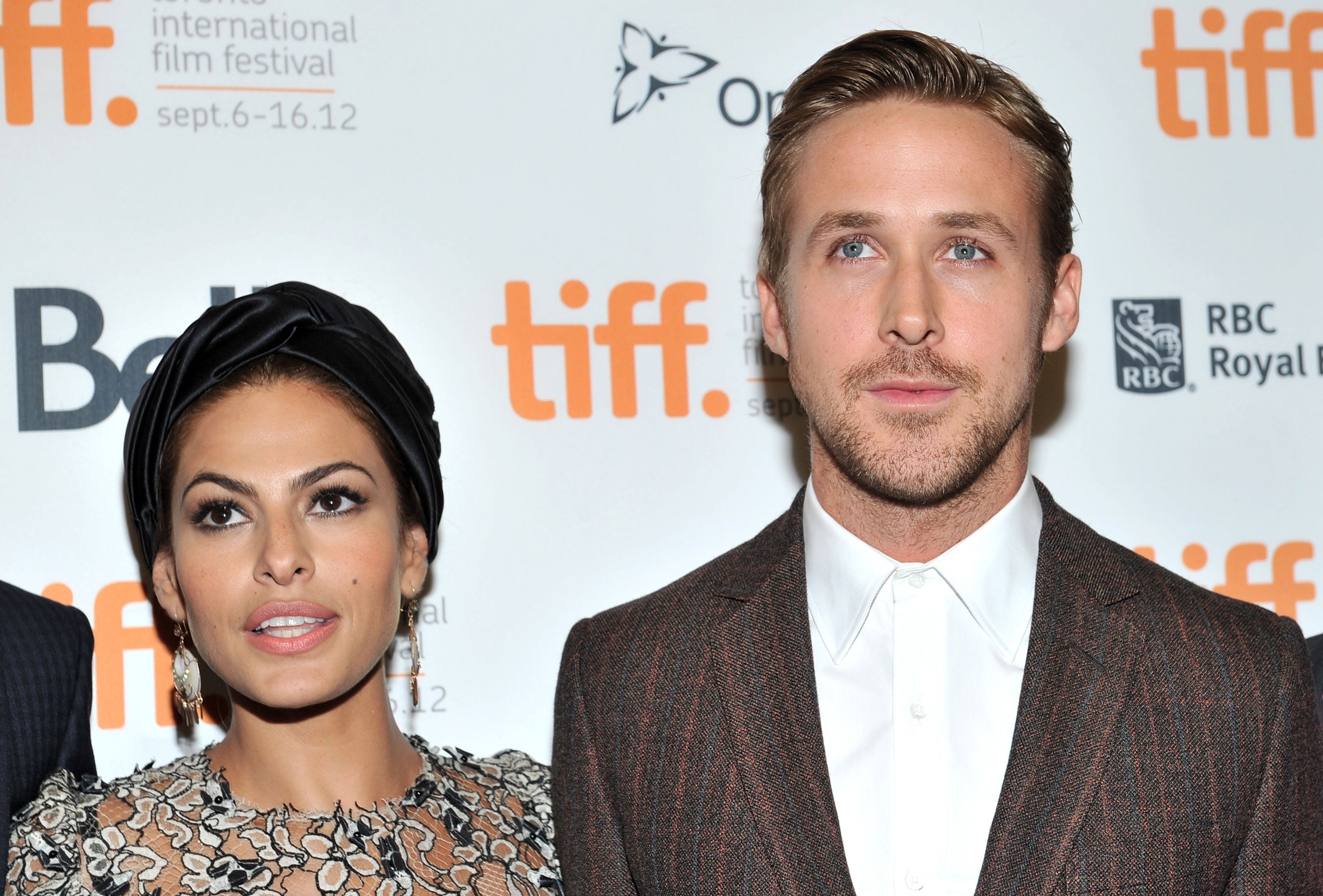 Two individuals at a film festival event; one in a floral dress with a head wrap, and the other in a brown suit with a white shirt