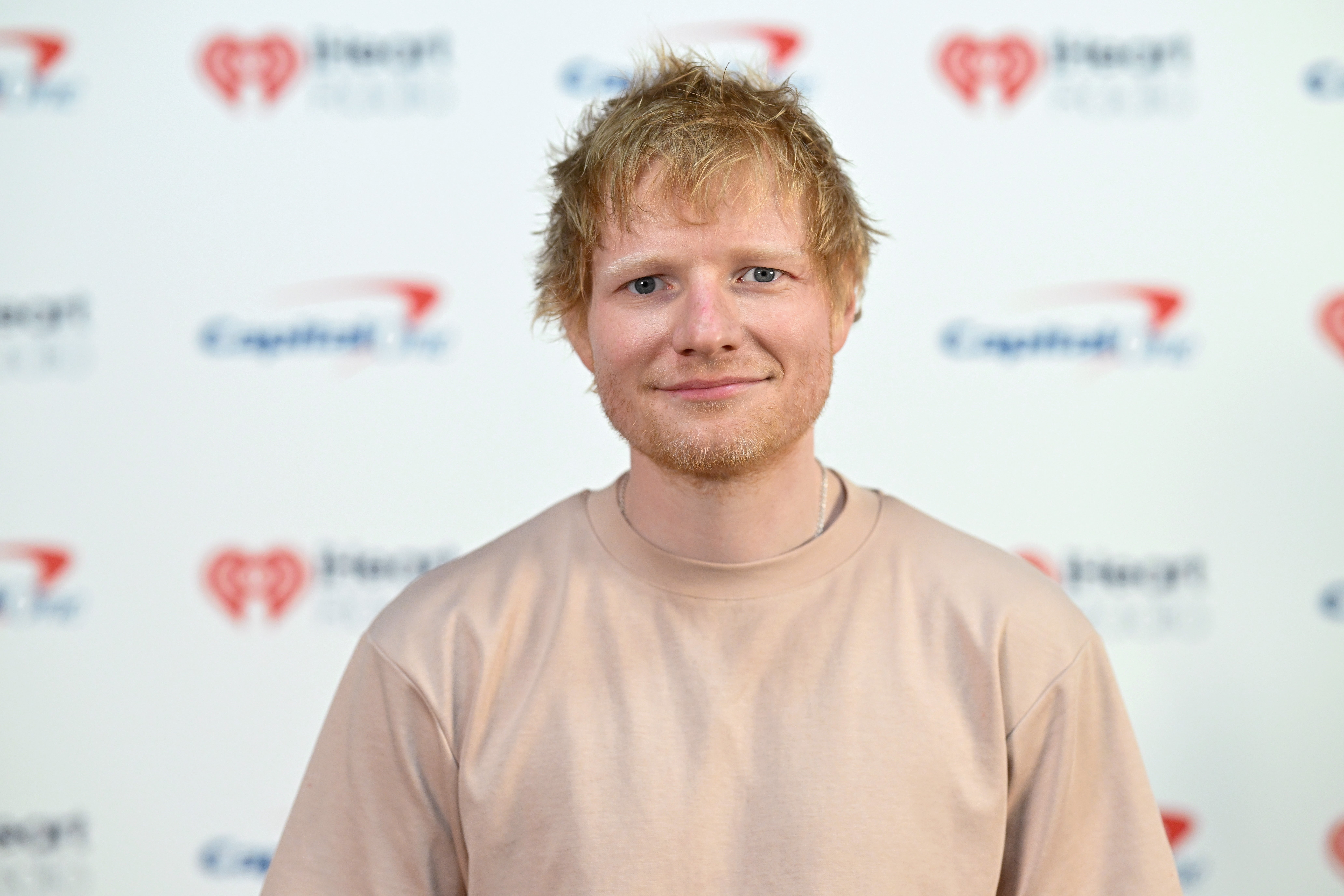 Person in a casual shirt smiling at an event with a media backdrop featuring logos