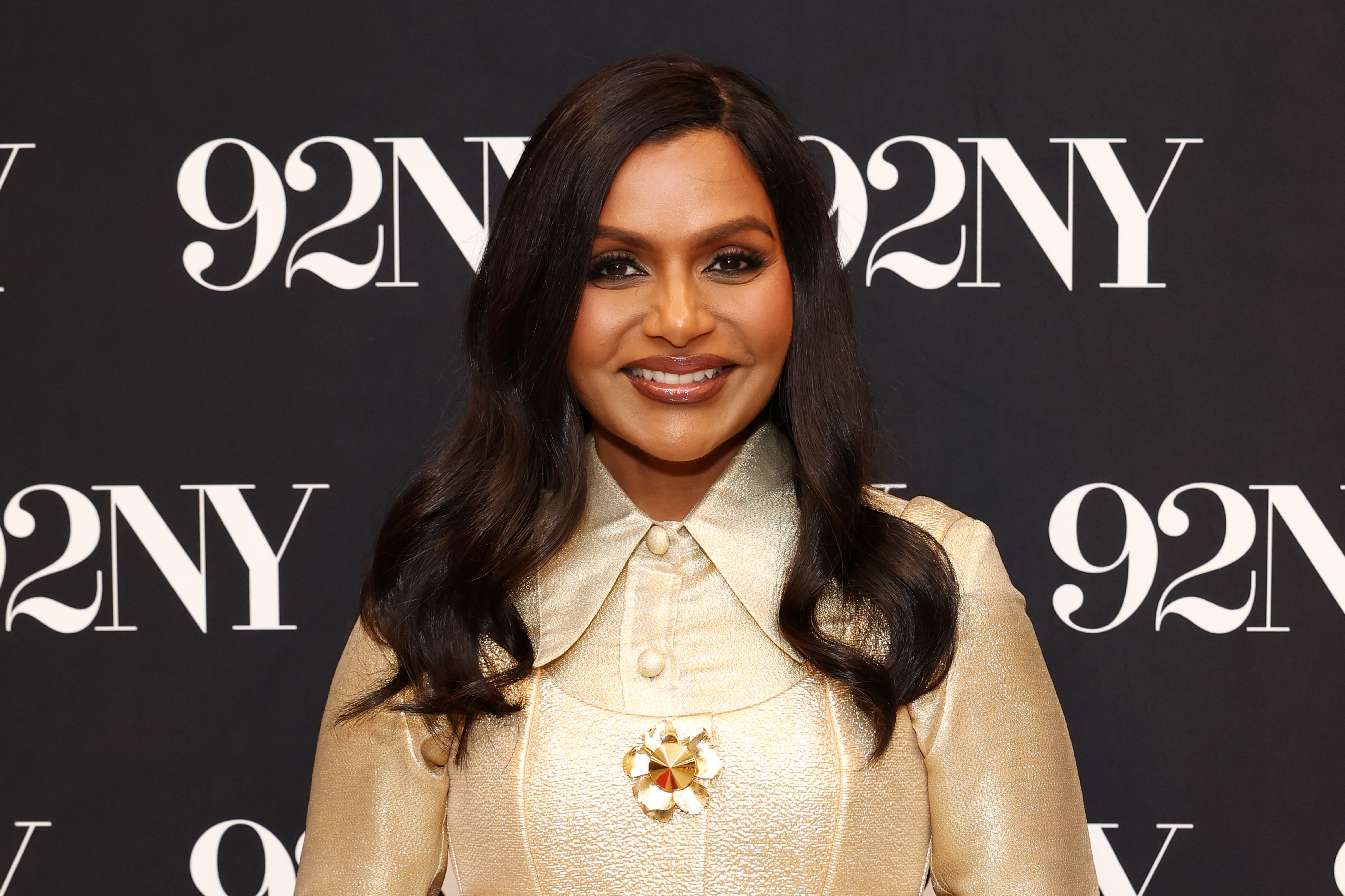 Person in glamorous attire with long sleeves and a decorative collar stands smiling at an event with "92NY" in the background