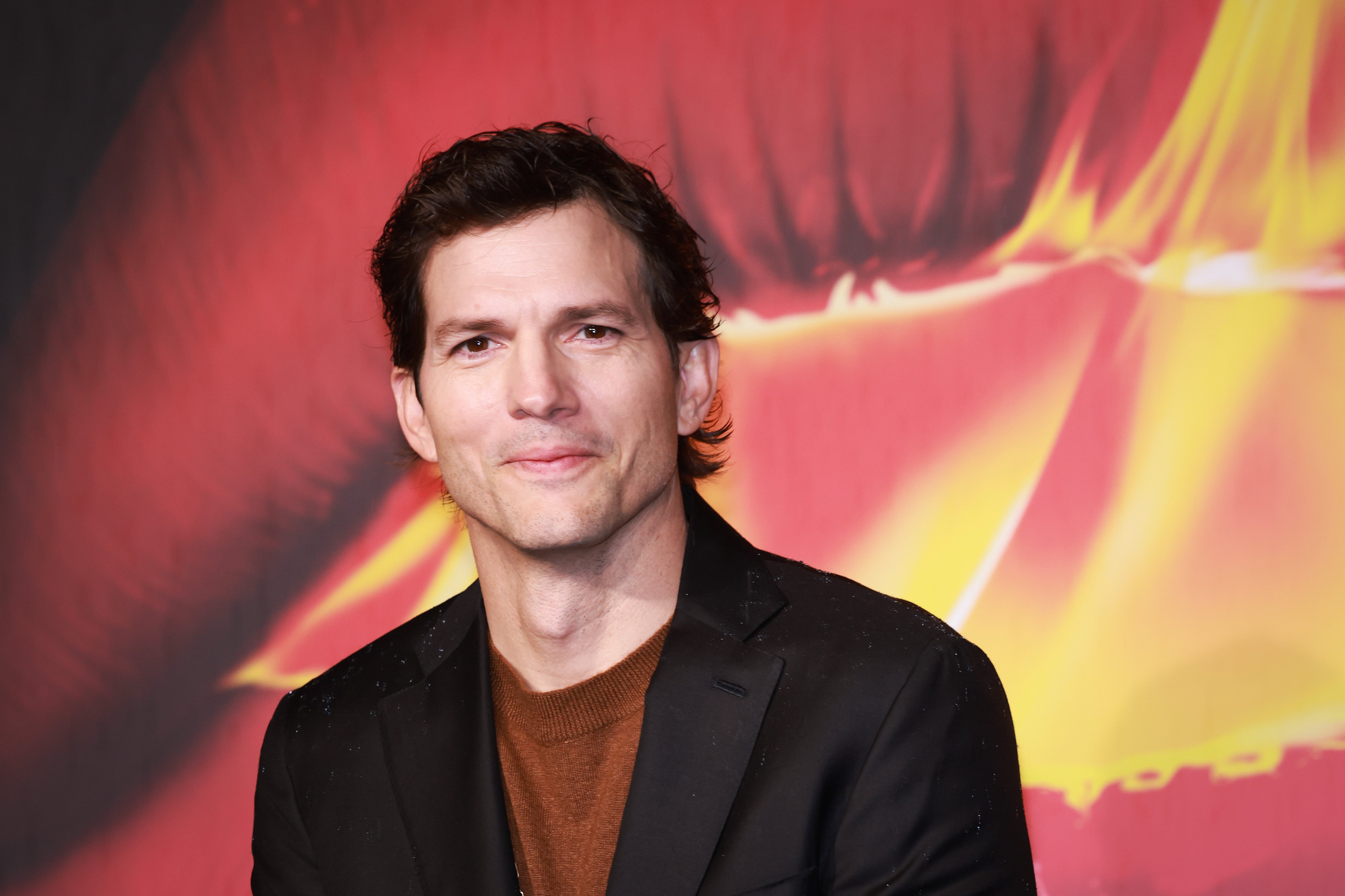 A person in a suit poses in front of a vibrant, abstract background featuring large lips
