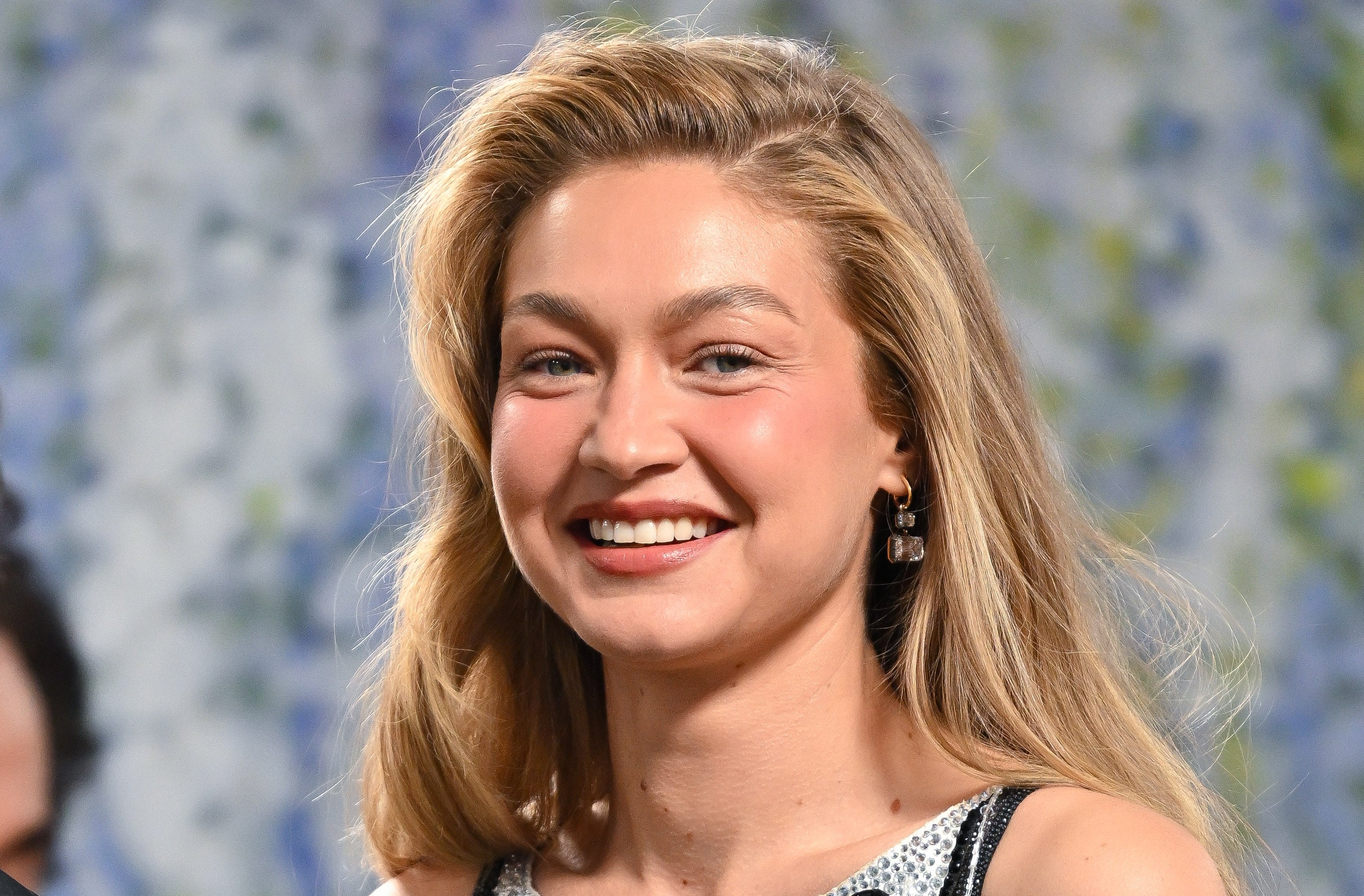 Person smiling at an event, wearing sleeveless attire with earrings, against a blurred background