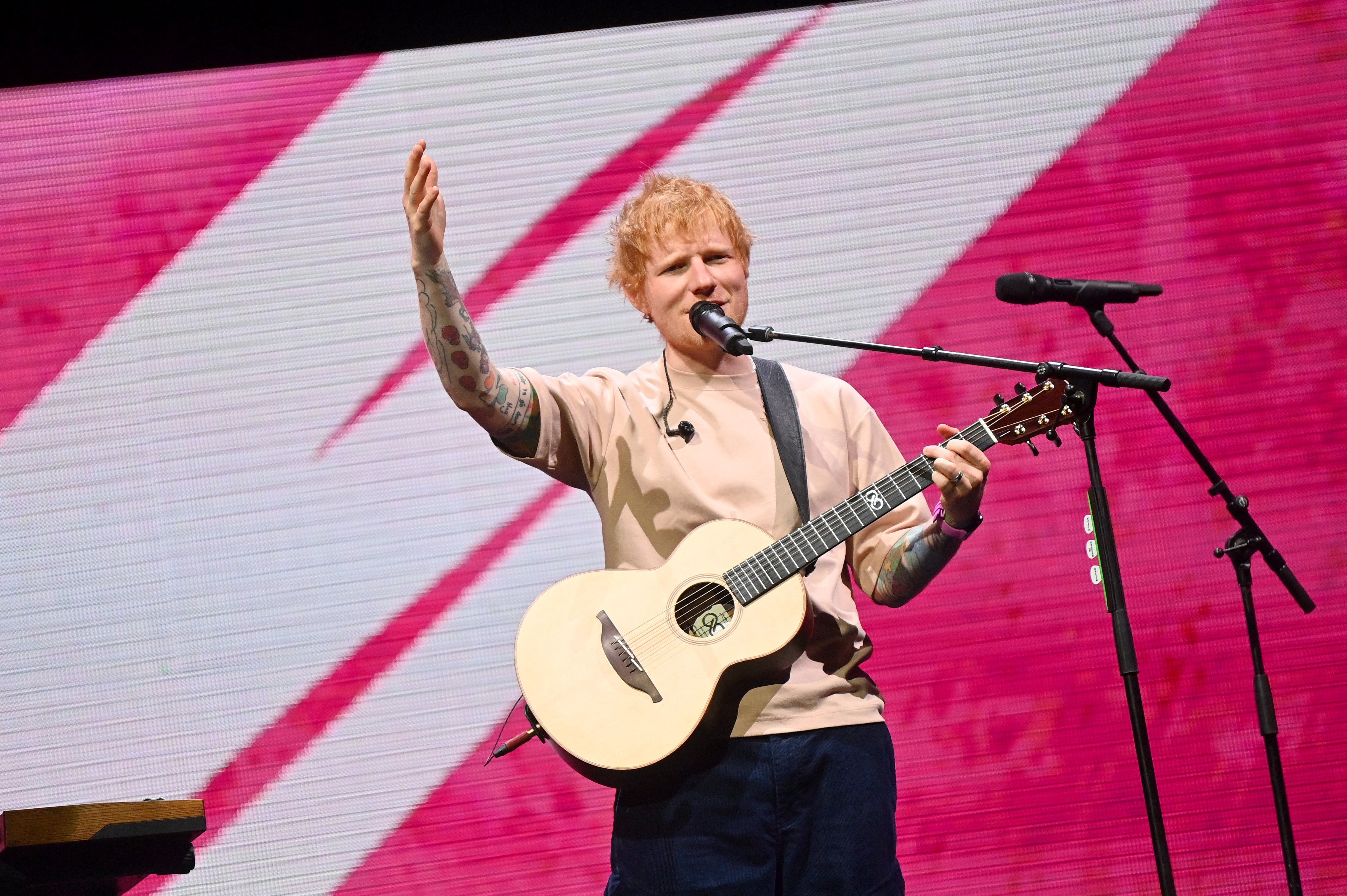 Musician on stage with a guitar, performing passionately with one hand raised, against a dynamic background