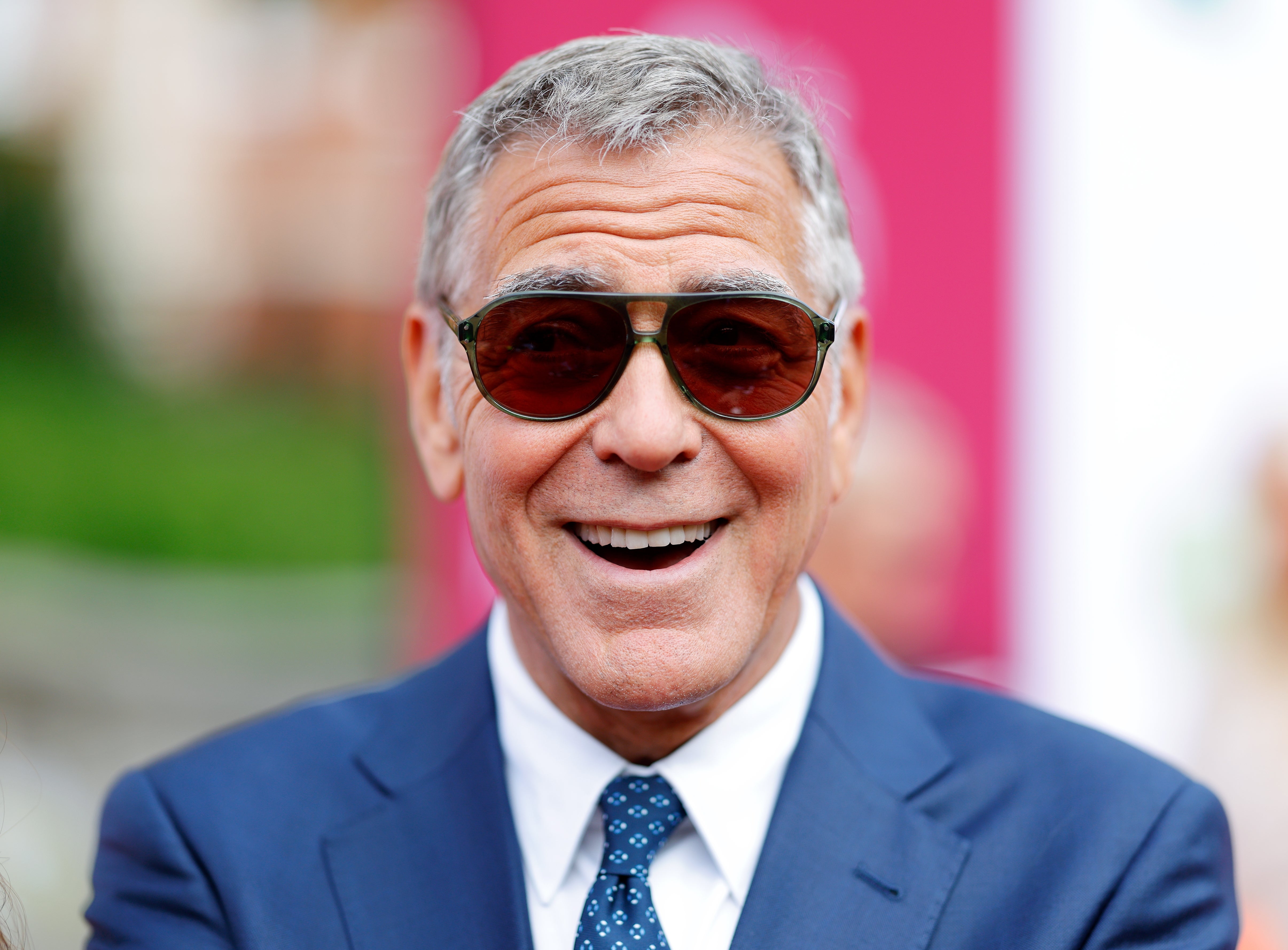 Man in sunglasses smiling, wearing a suit with a tie