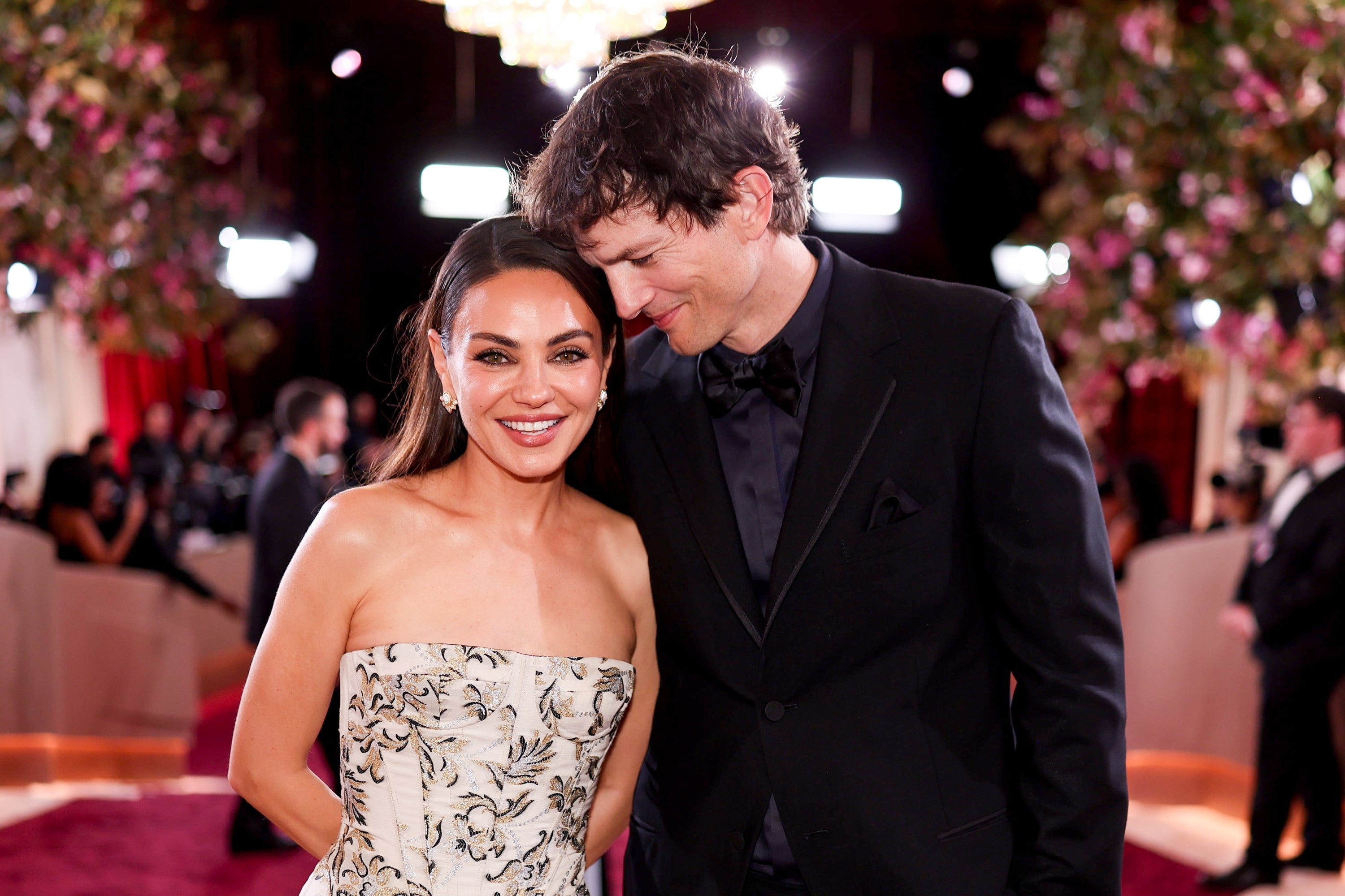 A man and woman smiling at an event, the woman in a strapless floral gown, the man in a dark suit