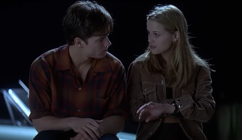 A couple sits closely, looking into each other's eyes, in an intimate moment by the water at night