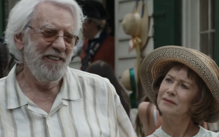 Two people in casual, vintage-style clothing, one wearing a straw hat, at an outdoor social event