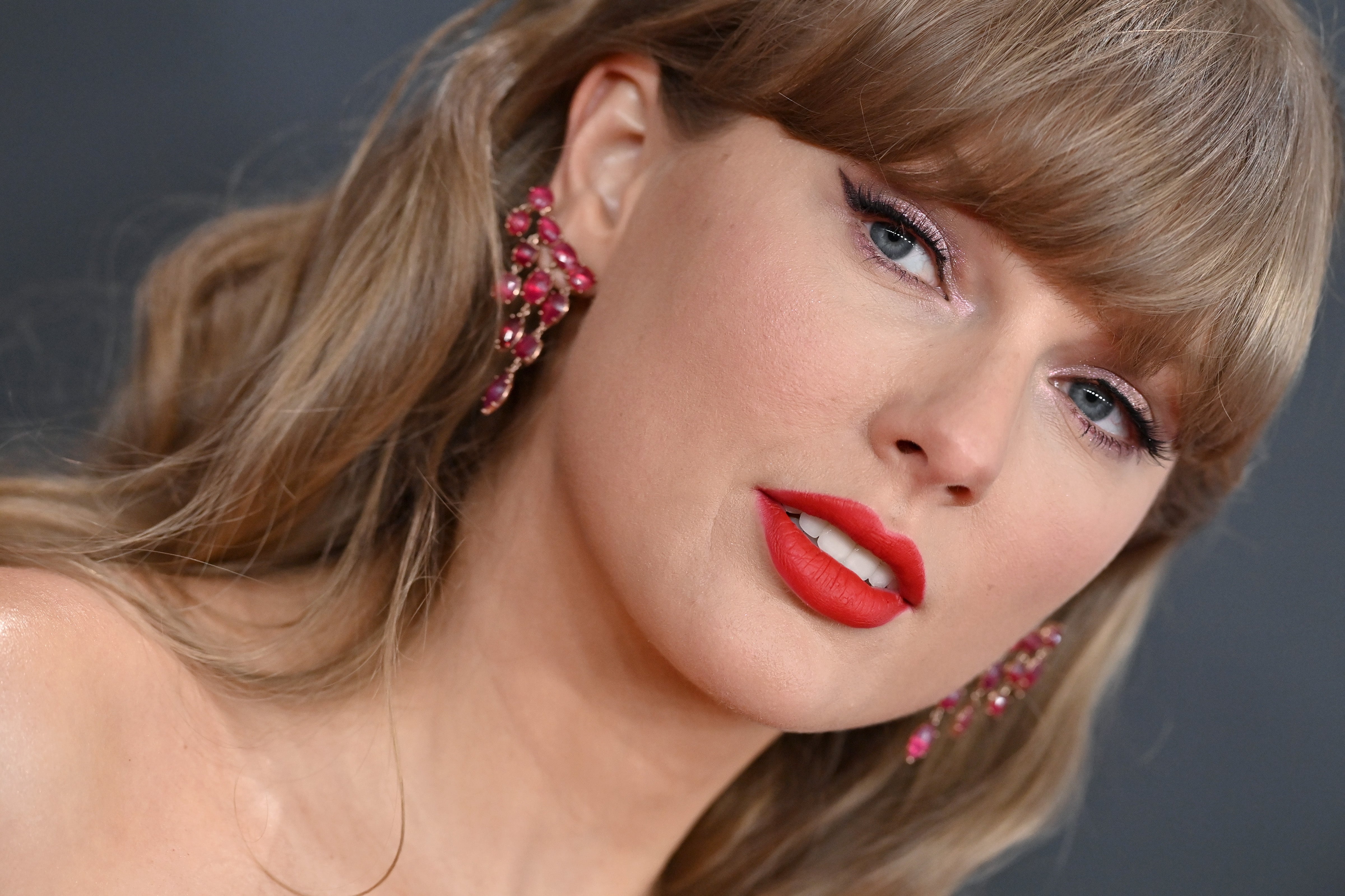 Taylor Swift posing astatine  an event, wearing elegant earrings and bold makeup, with a assured  expression