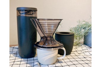 コーヒードリッパー、マグカップ、キャニスターなどがチェック柄の布の上に置かれている
